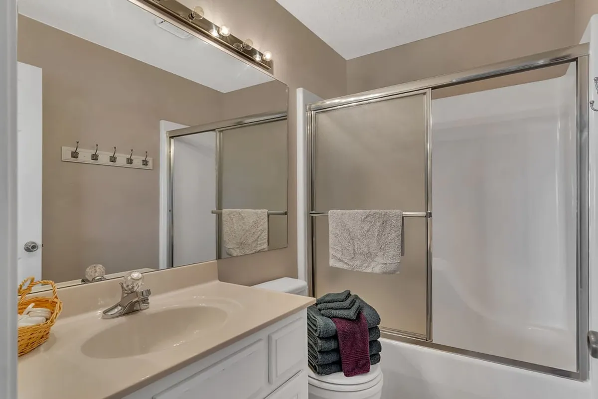 A bright, organized bathroom featuring a modern vanity with a sink, a mirrored wall, a shower area, fresh towels, and a basket of toiletries designed for self-care and relaxation.
