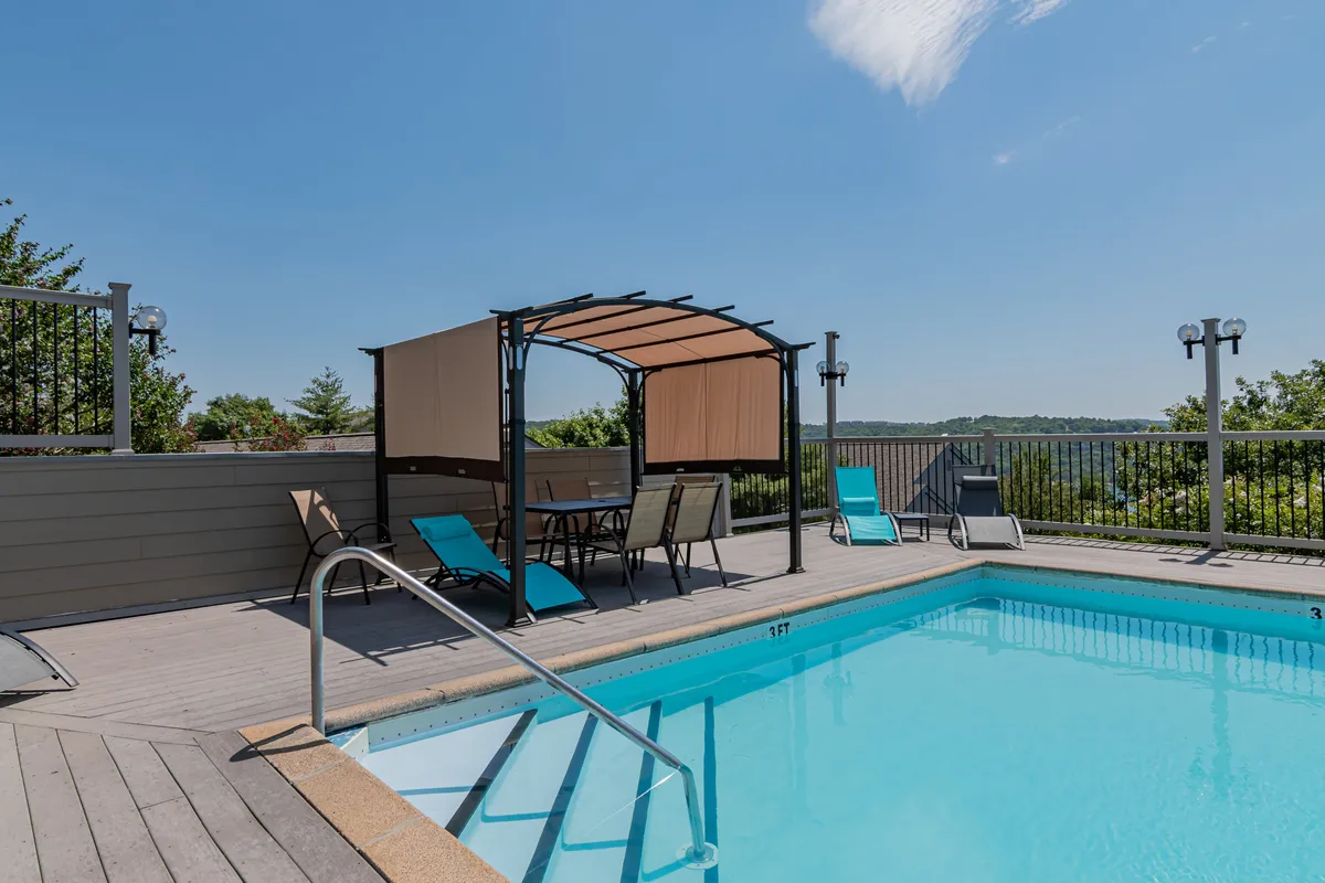 An inviting exterior shot of a sparkling swimming pool surrounded by lounge chairs and a canopy seating area, all set against a scenic landscape backdrop. The scene captures a leisurely atmosphere ideal for relaxation after a busy day out.