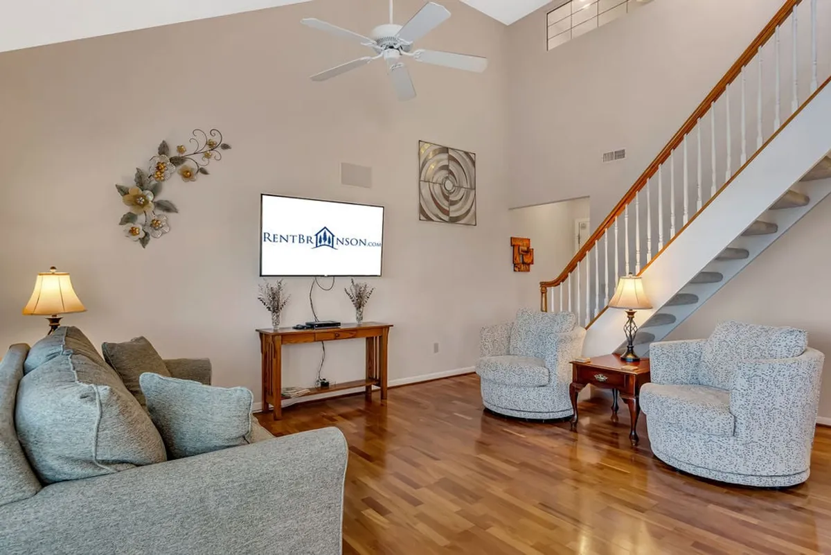 This image features a spacious living area with a sofa, television, armchairs, and a visible staircase, creating an inviting atmosphere for relaxation, group gatherings, and entertainment. The seating arrangement is ideal for socializing or watching television, and the open layout offers flexibility for various activities.