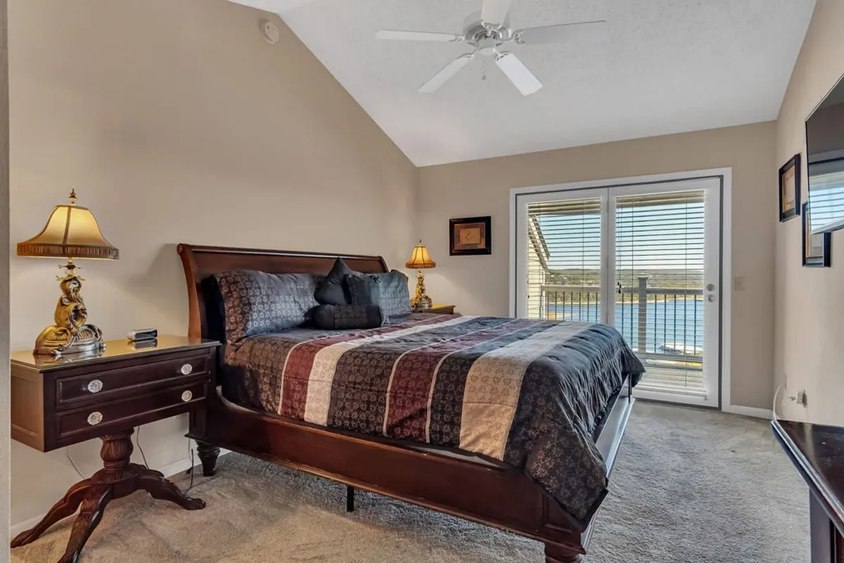 A serene bedroom scene with a cozy bed, sliding doors that likely lead to a deck or balcony, a nightstand, and a lamp—perfect for enjoying natural views or a quiet evening indoors.