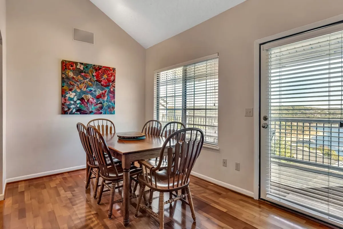 The image showcases a stylish dining area with a spacious table set for family meals, vibrant artwork on the wall, and a large window that fills the room with natural light and hints at beautiful views beyond. The inviting setup suggests comfort and togetherness, ideal for group gatherings.