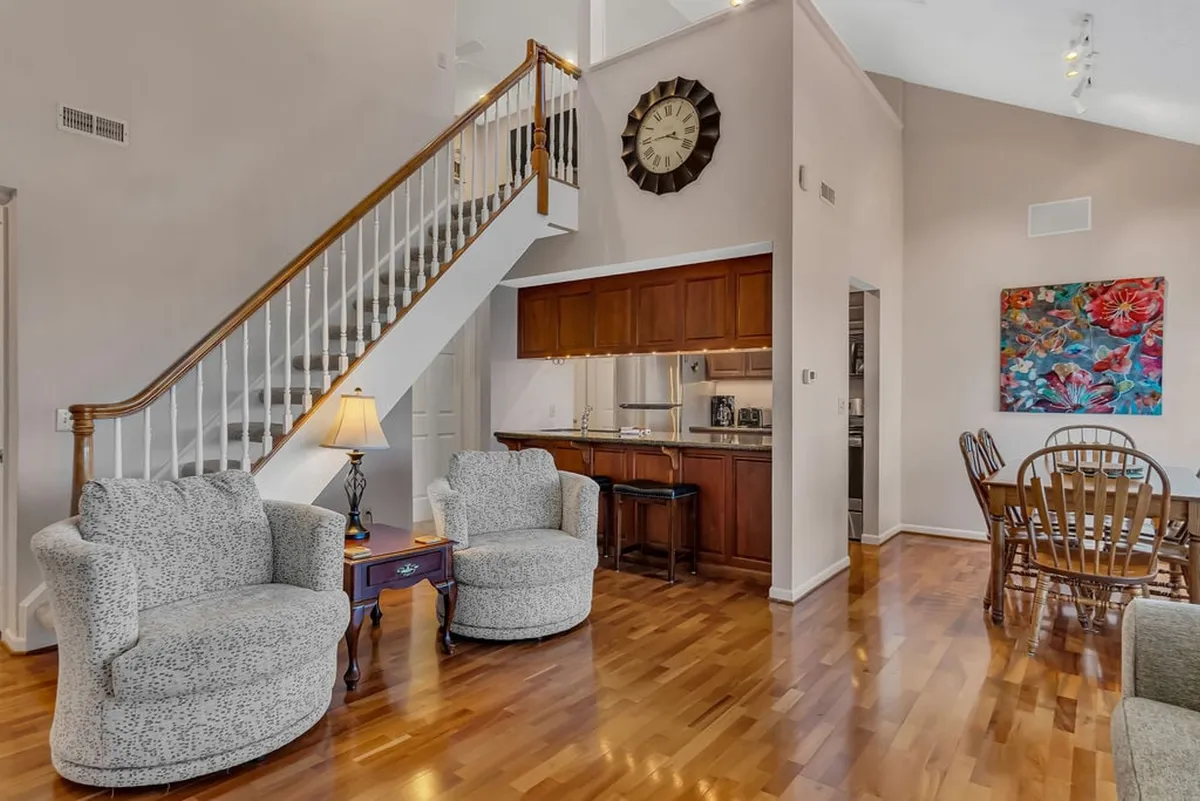 A wide-view interior featuring a staircase, seating area, dining table, and kitchen area, with stylish wall art—set up for comfortable group socializing, dining, and entertainment.