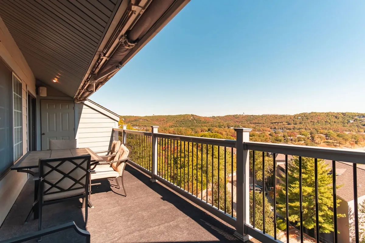 A serene balcony scene with a table and chairs overlooking distant hills. The setting evokes relaxation and togetherness, inviting guests to enjoy fresh air, beautiful views, and al fresco dining or morning coffee with friends and family.