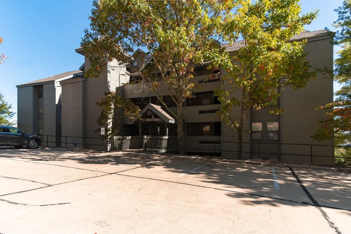 This exterior shot showcases the building entrance framed by mature trees and a convenient parking area. The setting is peaceful and welcoming, hinting at easy access for boats and trailers and the community feel of the resort.