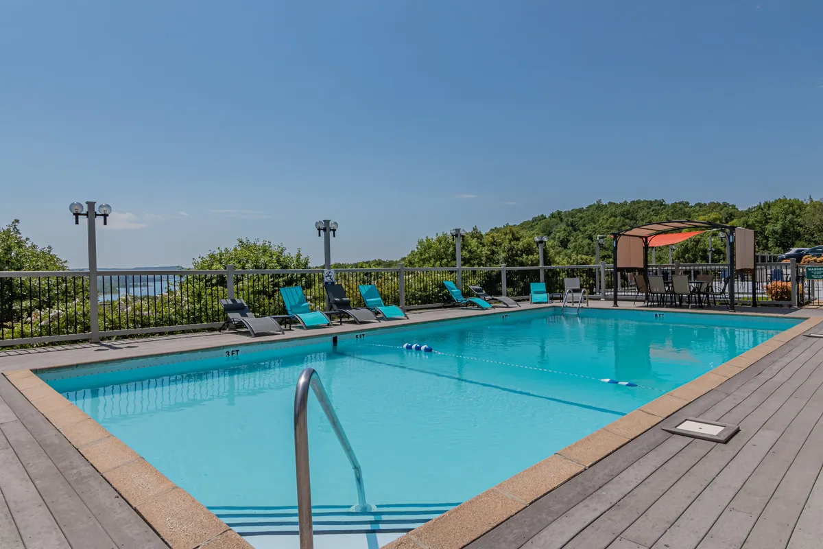 The scene features an inviting swimming pool bordered by lounge chairs and a shaded canopy area. The pool is bathed in natural light, perfect for relaxing, socializing, or cooling off after a day on the lake.